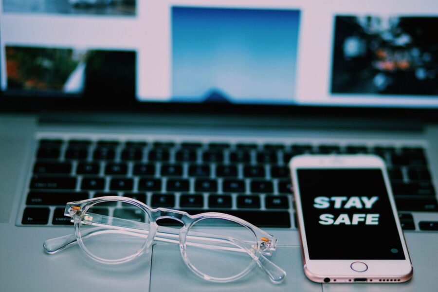 High angle of modern cellphone with Stay safe on screensaver and netbook with glasses placed above